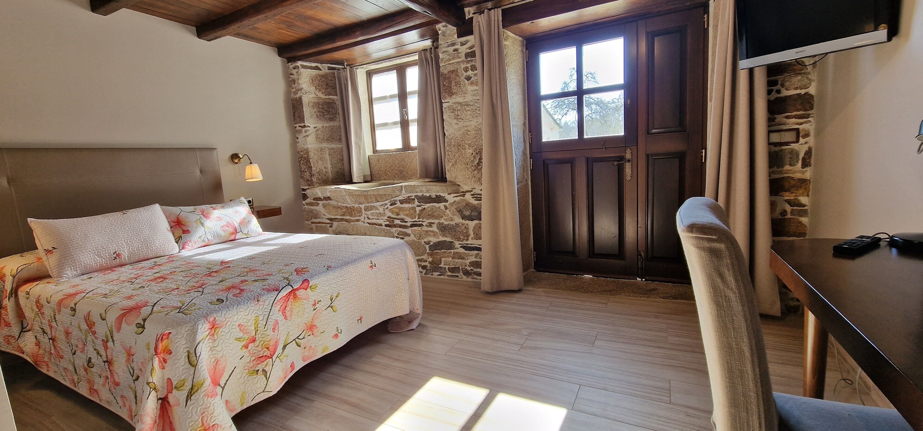 A bedroom with a bed, a desk, a chair, a TV, and a stone wall.