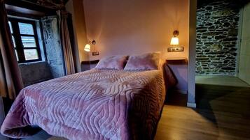 A bedroom with a bed, two bedside lamps, a stone wall, and a window.