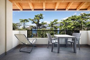 A balcony with a table and chairs, a wooden ceiling, and a view of trees and mountains. - The essence apartments n15 (Malcesine)