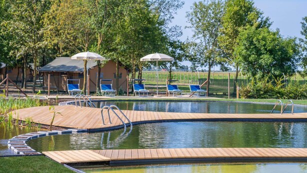 A swimming pool with a wooden deck, lounge chairs, and umbrellas. - Tenuta Regina Agriturismo e Glamping (Palazzolo dello Stella)