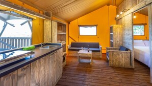 A cozy cabin interior with a wooden floor, a kitchenette, a seating area with a bench, and a window providing natural light. - Tenuta Regina Agriturismo e Glamping (Palazzolo dello Stella)