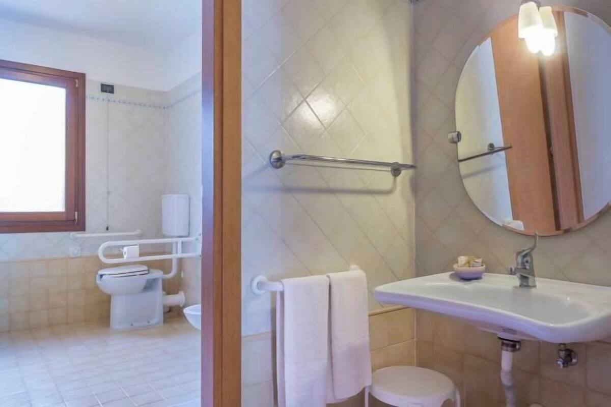 A bathroom with a toilet, sink, mirror, towel rack, and a window.