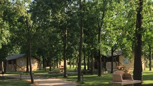 A campground with multiple cabins, a gravel path, and a barbecue grill. - Tenuta Regina Agriturismo e Glamping (Palazzolo dello Stella)
