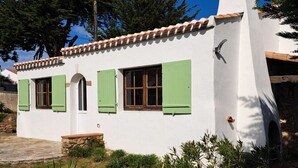 Un edificio blanco con contraventanas verdes, una chimenea de piedra y una escalera de piedra que lleva a la entrada.