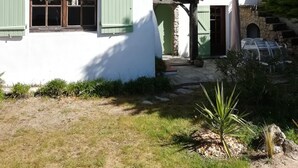 Un edificio blanco con contraventanas verdes, techo de tejas y una escalera de piedra que lleva a una puerta.