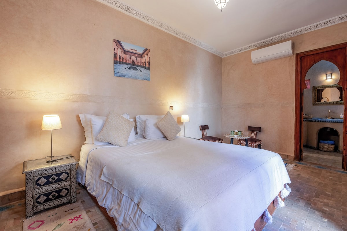 A large bed with a white bedspread, two bedside lamps, and a decorative nightstand.