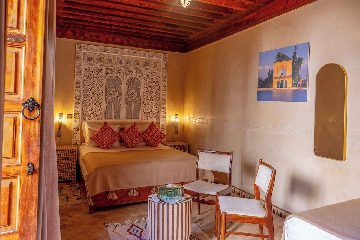 A bedroom with a large bed, a chair, a small table, and a wall-mounted picture.