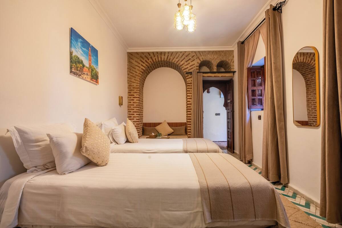 A hotel room with two beds, a painting on the wall, a chandelier, and a brick archway.