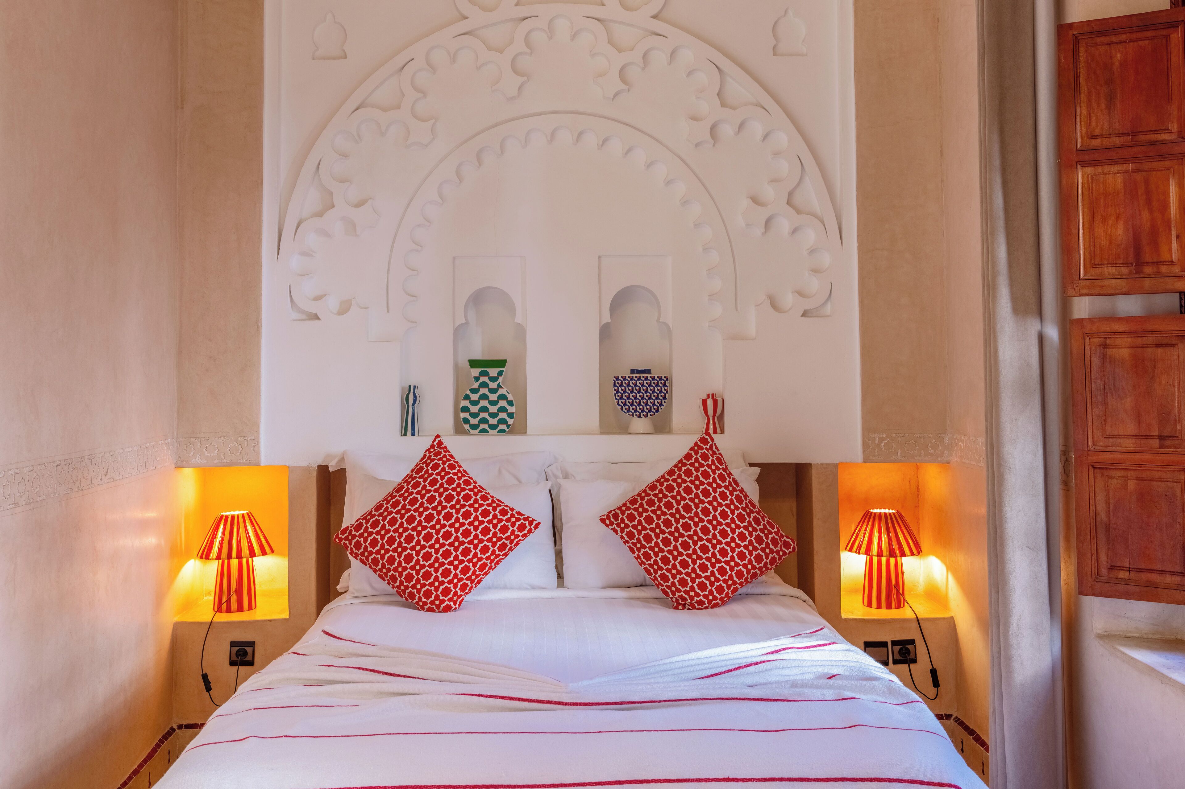 A hotel room with a bed, two bedside lamps, and a decorative wall arch.