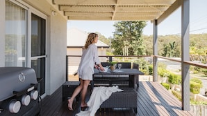 A balcony with a grill, wicker furniture, and a view of the surrounding landscape.