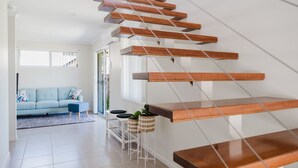 A modern staircase with wooden steps and metal railings, leading to a living area with a light blue sofa and a small side table with plants.