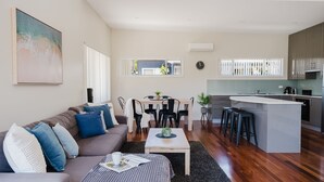 A modern living room with a sofa, coffee table, and dining area. There is a kitchen with a bar and stools.