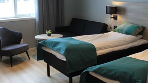 Habitación de hotel con dos camas individuales, una mesita redonda con una planta, una silla y un ventanal con cortinas.