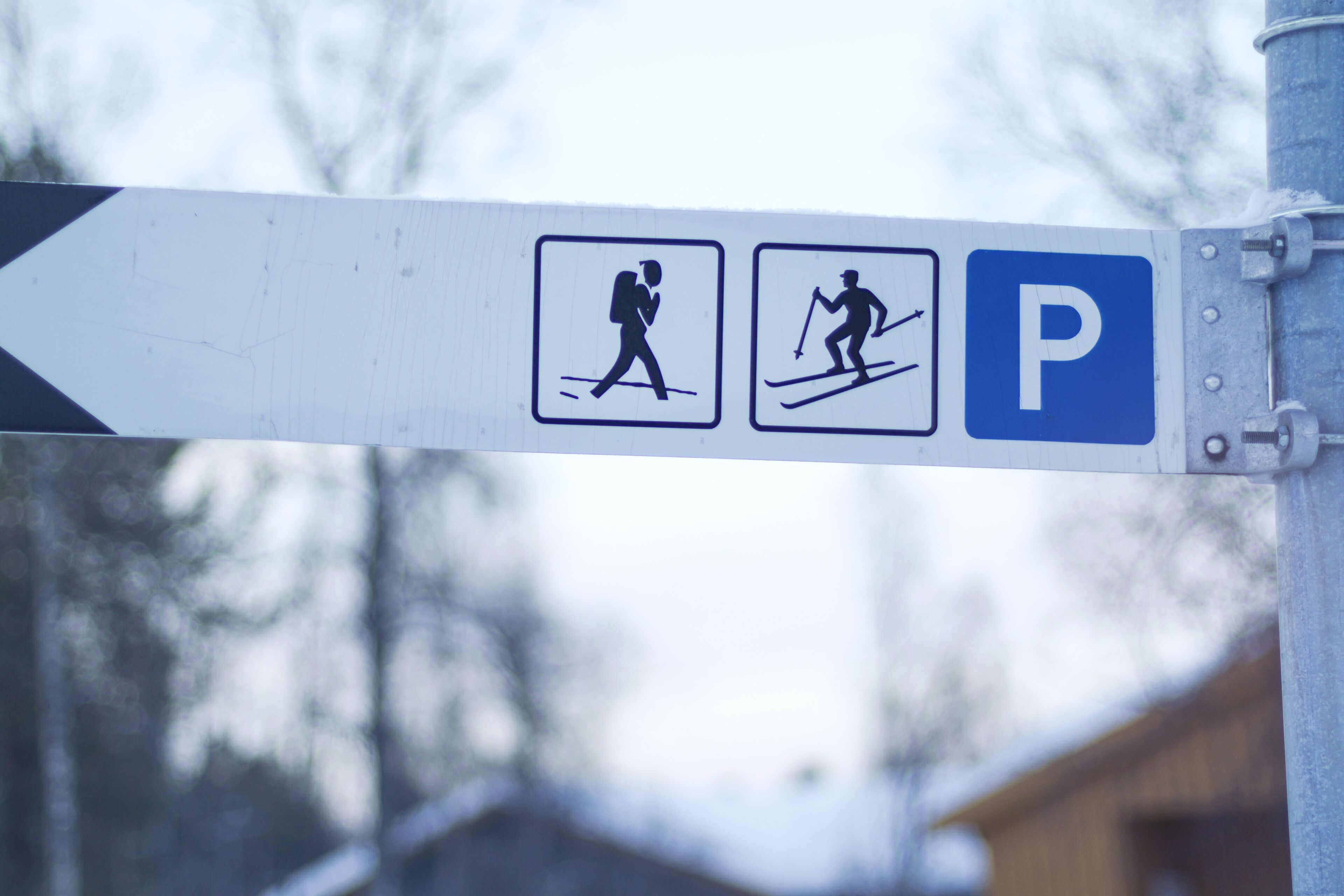 A directional sign with symbols for walking and skiing, and a parking symbol.