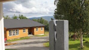 Una cabaña de madera con techo negro, un camino de entrada pavimentado y una gran escultura de piedra al frente.