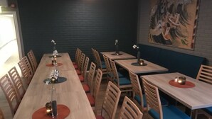 Un restaurante con largas mesas y sillas de madera, algunas con cojines azules. Hay velas en las mesas y un cuadro grande en la pared.