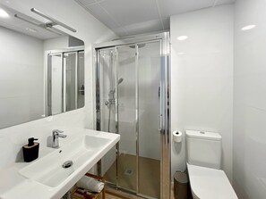 Ein modernes Badezimmer mit einer Duschkabine, einem weißen Waschbecken und einer Toilette.