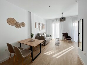 A modern living room with a dining area, featuring a wooden table, chairs, a sofa, and a coffee table. - Apartamento de un Dormitorio - Picú Home (Málaga)