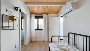 A bedroom with a bed, a small stool, a mirror, and a window with curtains. - Duplex de dos Dormitorios con Terraza - Picú Home (Málaga)