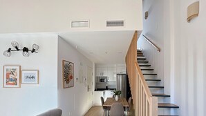 A modern kitchen with white cabinets, a stainless steel refrigerator, and a wooden staircase. - Duplex de dos Dormitorios con Terraza - Picú Home (Málaga)