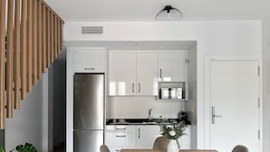 Eine moderne Küche mit weißen Schränken, einem Edelstahlkühlschrank und einer Mikrowelle. Ein Esstisch mit Stühlen und eine Blumenvase sind ebenfalls vorhanden.