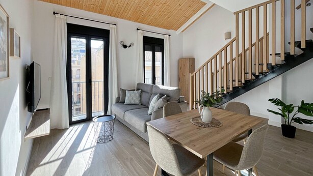 Ein modernes Wohnzimmer mit Holzboden, einer Treppe, einem Sofa, einem Esstisch und einem Fernseher.