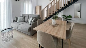 Ein modernes Wohnzimmer mit grauem Sofa, Esstisch aus Holz und einer Treppe.