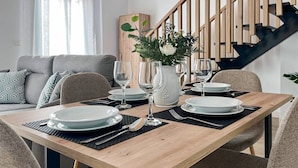 Ein Essbereich mit einem Holztisch, gedeckt für vier Personen, umgeben von grauen Sofas und einer Treppe im Hintergrund.