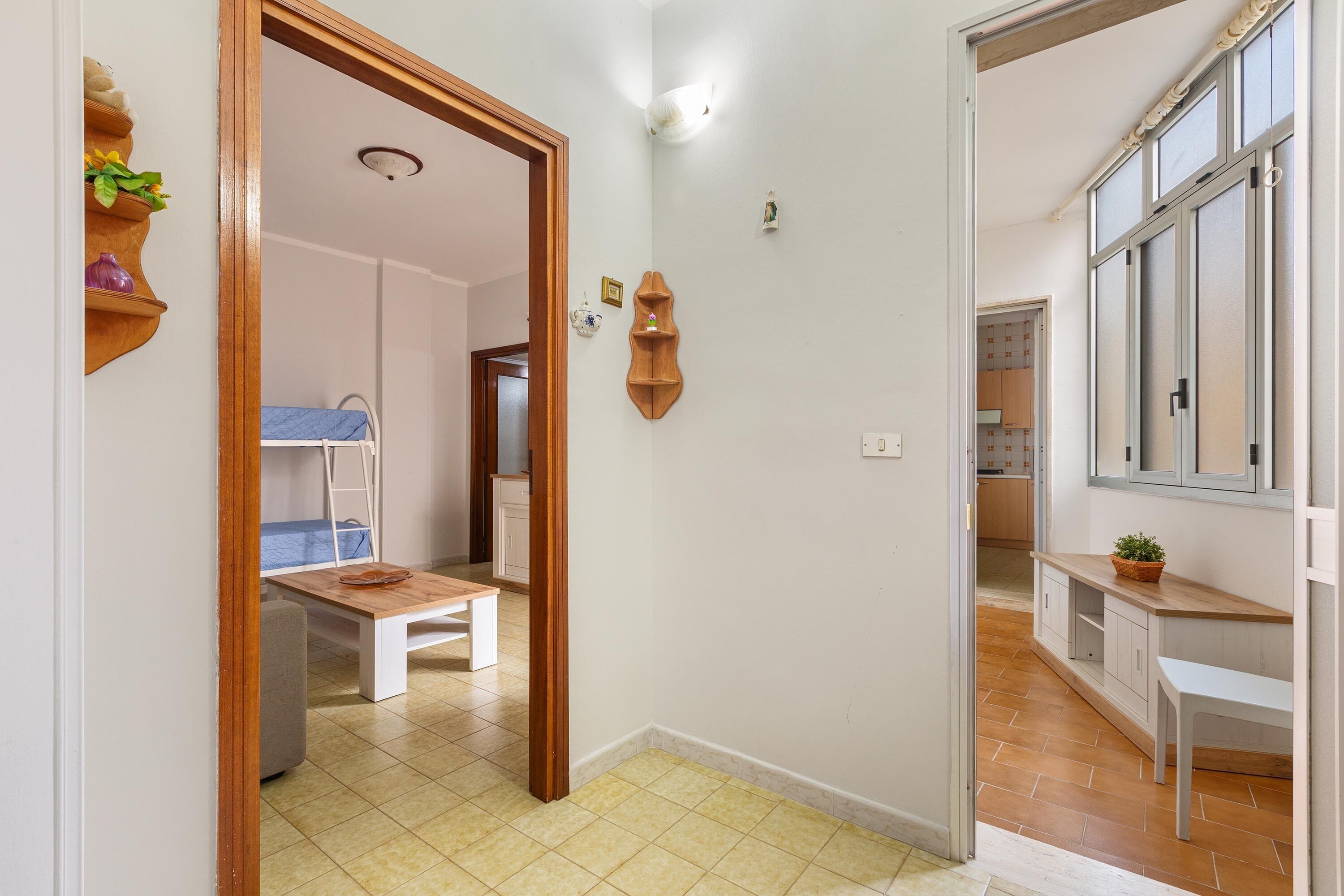 A narrow hallway with a wooden bench, a small table, and a wall-mounted shelf with decorative items.