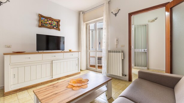 Ein Wohnzimmer mit Fernseher auf einer Holzkommode, einer Couch und einem Tisch mit einem dekorativen Gegenstand.