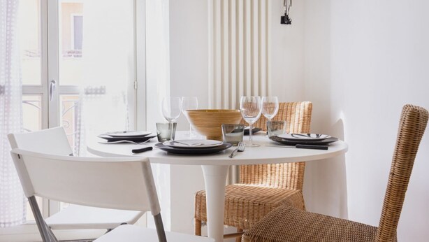 A round dining table with white chairs, a wicker chair, and a bowl. - Easylife - Spacious apartment in Porta Romana (Milano)
