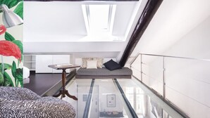 A modern room with a glass floor, a bed with striped bedding, a small table, and a window with a view of the city. - Easylife - Spacious apartment in Porta Romana (Milano)