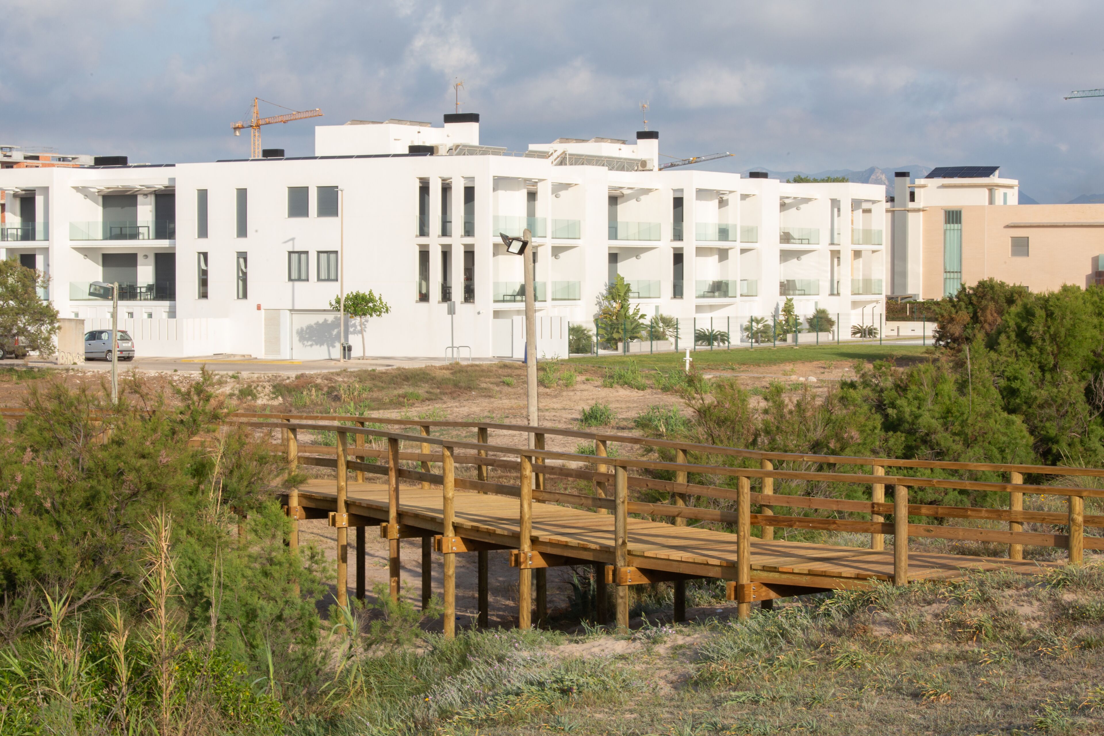 Ein modernes Gebäude mit mehreren Balkonen, einer Holzterrasse und einem Baukran im Hintergrund.