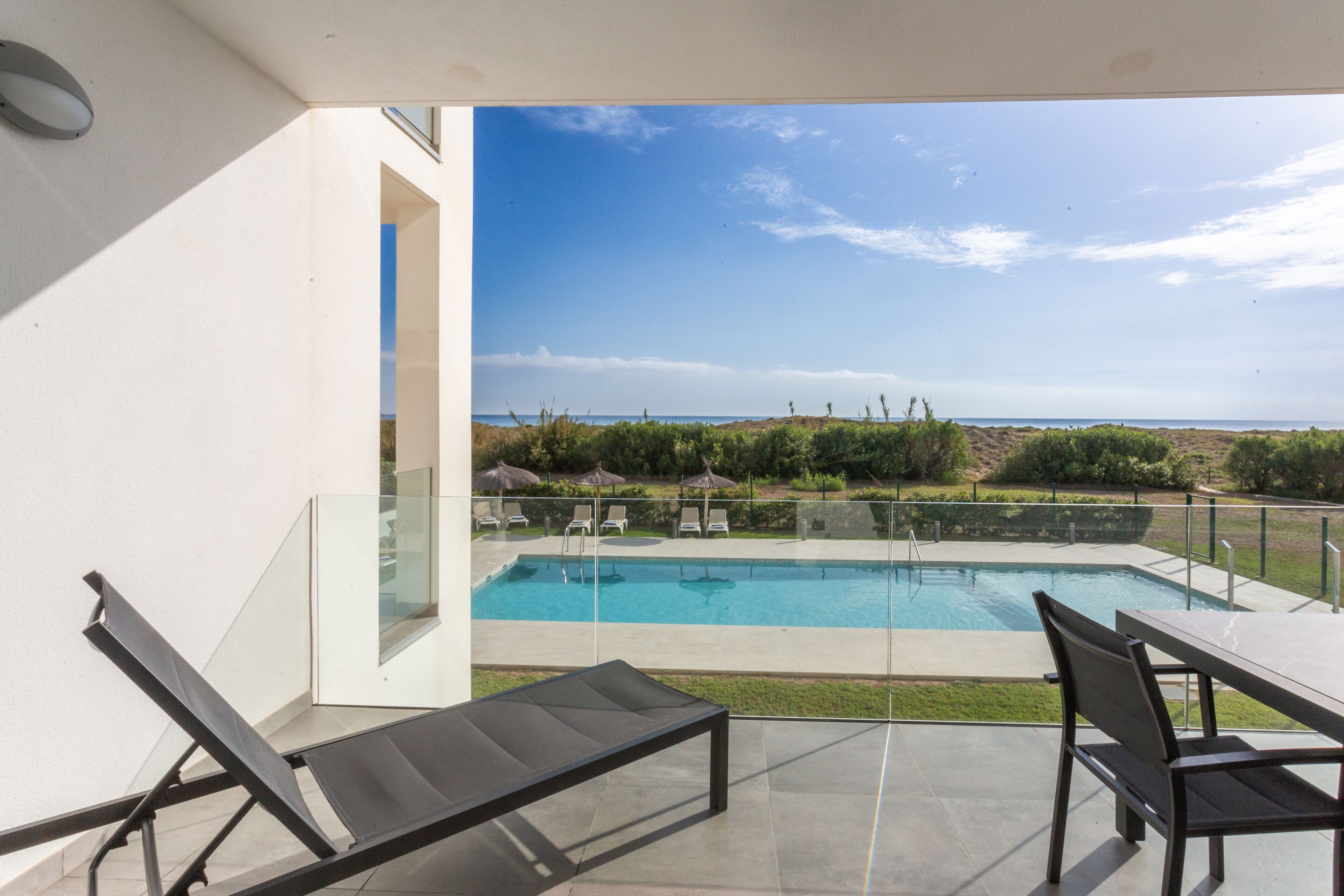 Ein moderner Poolbereich im Freien mit Liegestühlen und einem Tisch, mit Blick auf einen klaren Himmel und eine entfernte Landschaft.