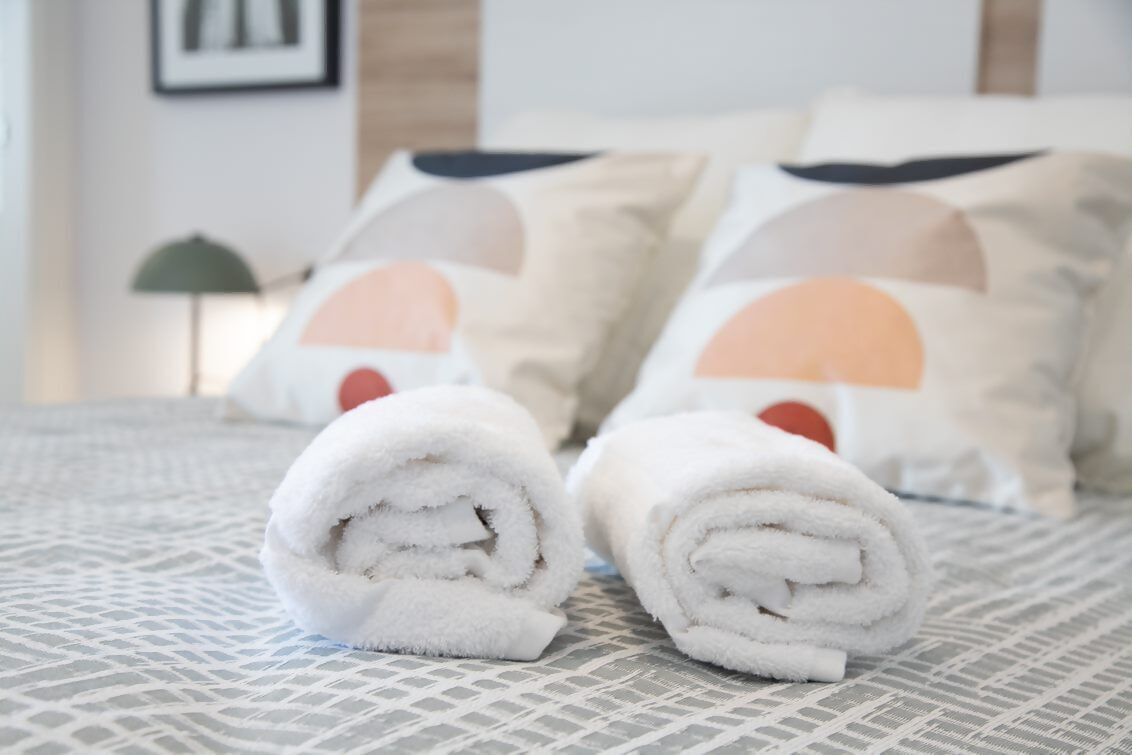 A neatly made bed with rolled white towels and pillows featuring a geometric design.