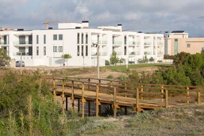 En moderne bygning med flere balkoner, et træterrasse og en byggekran i baggrunden.