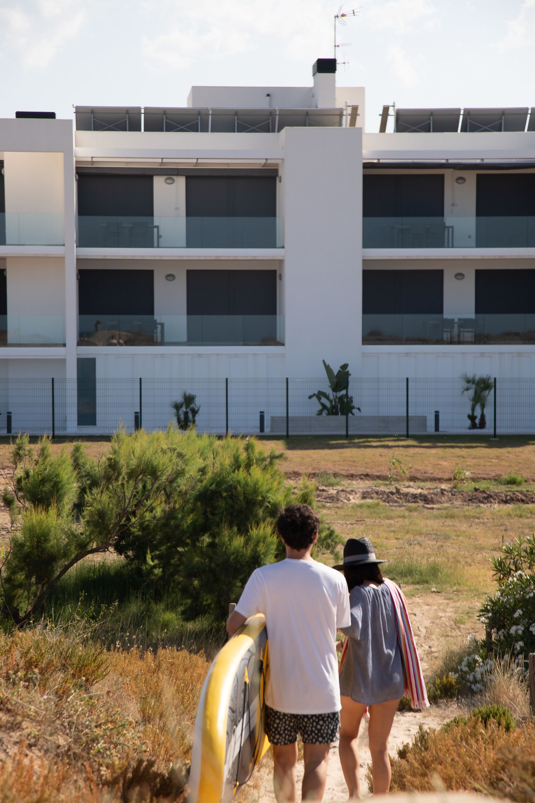 A modern building with multiple balconies and a fenced area with plants.