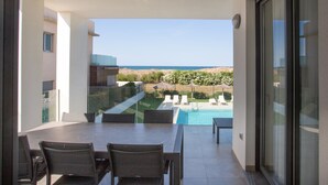 Un balcon avec une table et des chaises, donnant sur une piscine et un jardin aménagé.
