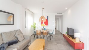 Un salon moderne comprenant un canapé, une table à manger, des chaises, un téléviseur et une console rouge.