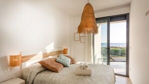 Une chambre à coucher comprenant un lit, des tables de chevet, un luminaire suspendu, une fenêtre avec vue et une porte donnant sur un espace extérieur.