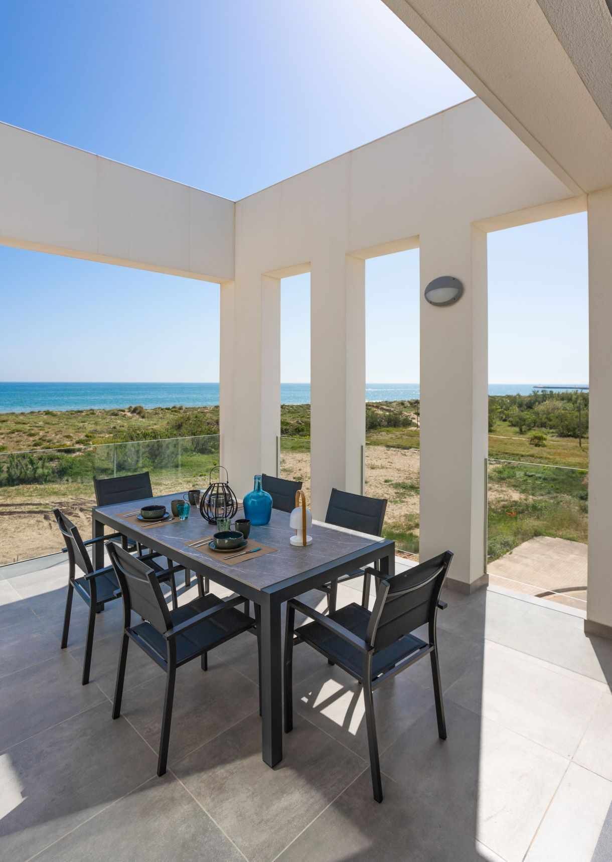 Un espace repas comprenant une table et des chaises, de grandes fenêtres et une vue sur la plage et l’océan.