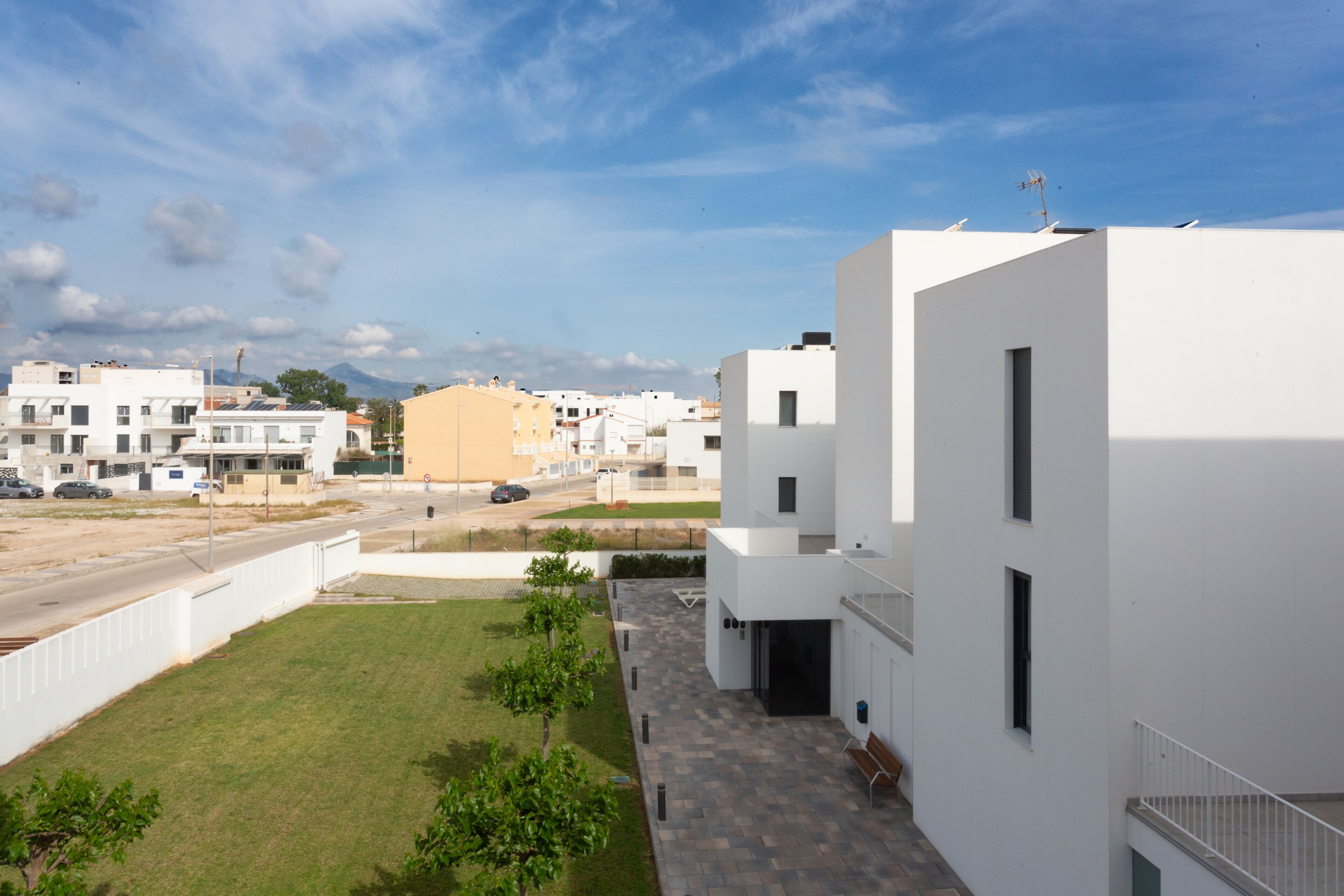 A modern building with a flat roof, a paved courtyard, and a clear sky.