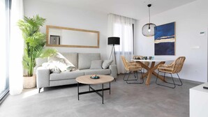 Ein modernes Wohnzimmer mit einem grauen Sofa, einem runden Couchtisch und Korbstühlen.