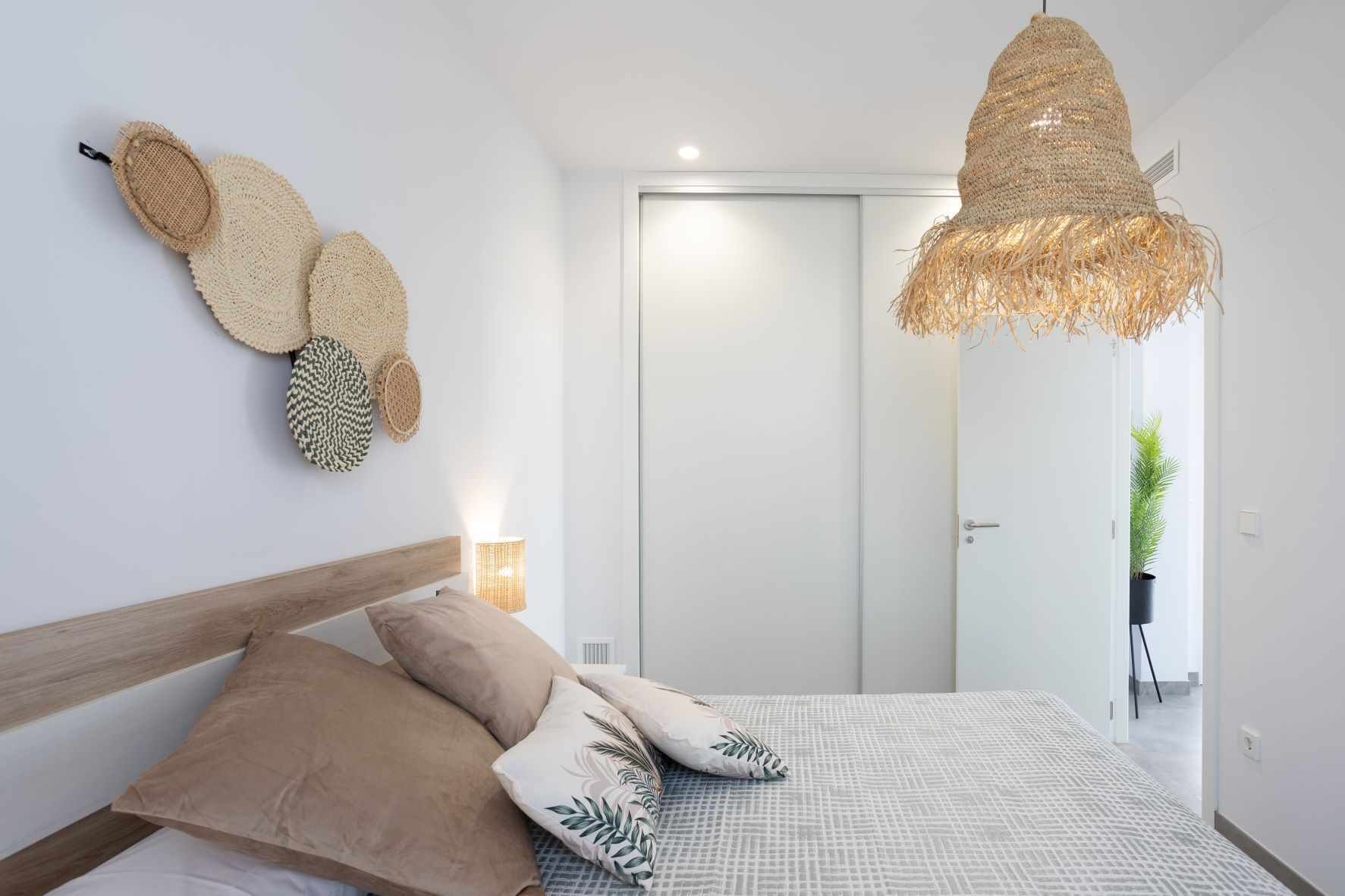 A modern bedroom with a wooden headboard, a patterned bedspread, and a woven hanging light fixture.
