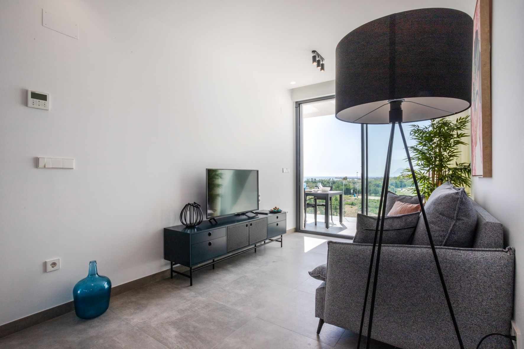 Ein modernes Wohnzimmer mit einem Flachbildfernseher, einer dunklen Ablage, einer blauen Vase und einer Stehlampe.
