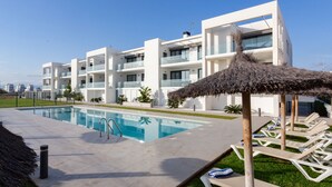 Un hôtel moderne doté d’une piscine, de chaises longues et d’un parasol en chaume.