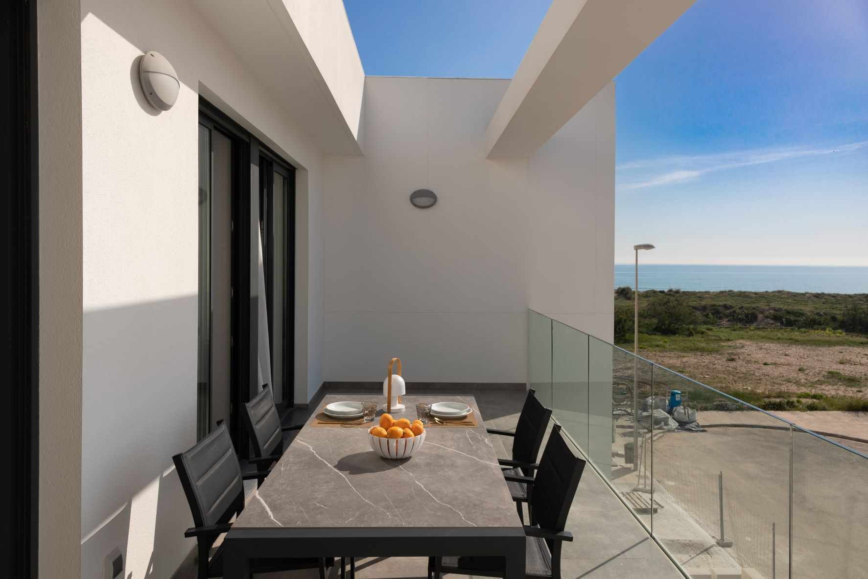 Un balcon avec une table à manger dressée pour deux personnes, un panier de fruits et une vue sur la mer.