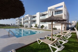 Ein modernes Hotel mit Swimmingpool, Liegestühlen und einem Strohdachschirm.