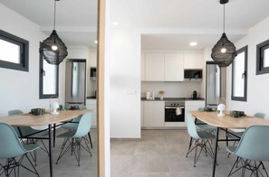 Eine moderne Küche mit weißen Schränken, Edelstahlgeräten und einem Essbereich mit einem Holztisch und blauen Stühlen.