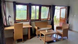 A room with a wooden desk, two wicker chairs, a small table, and large windows with curtains. - ilasan cottage (Tomohon)